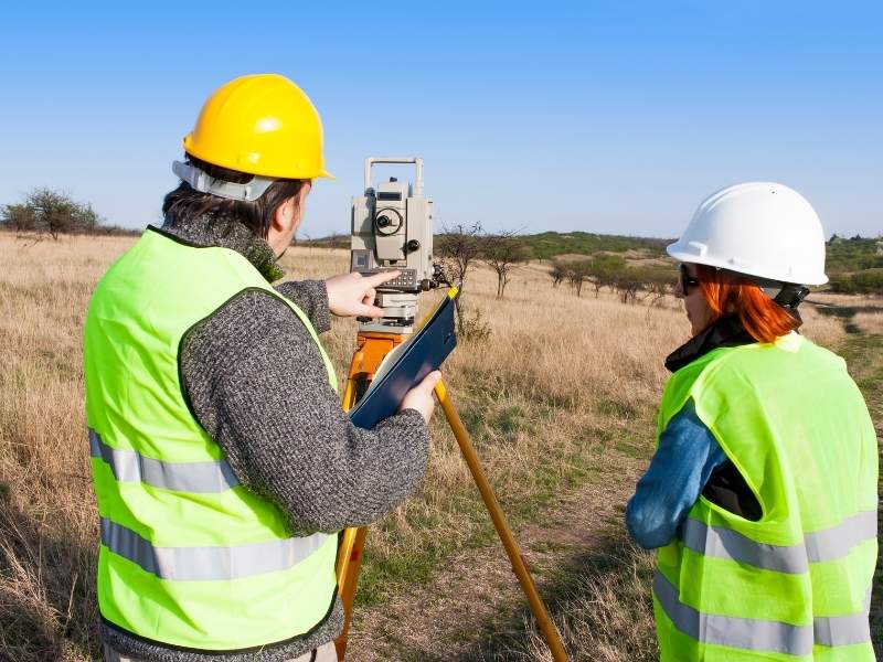 Licensed land surveyor reviewing measurements while operating surveying equipment in an open field