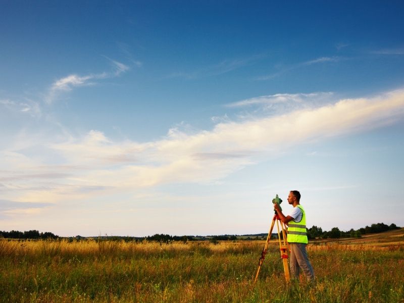 Surveyor using professional equipment to verify a property line boundary across an open field
