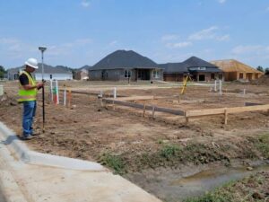 Foundation layout stakes tied to subdivision control on a graded residential lot with curbs, utility stubs, and drainage areas.
